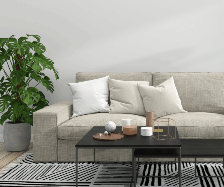 Modern neutral living room with a light beige sofa, minimal throw pillows, and black coffee tables styled with simple decor. A bold geometric rug and large potted plant add texture and contrast to the small space, making it feel stylish and open.