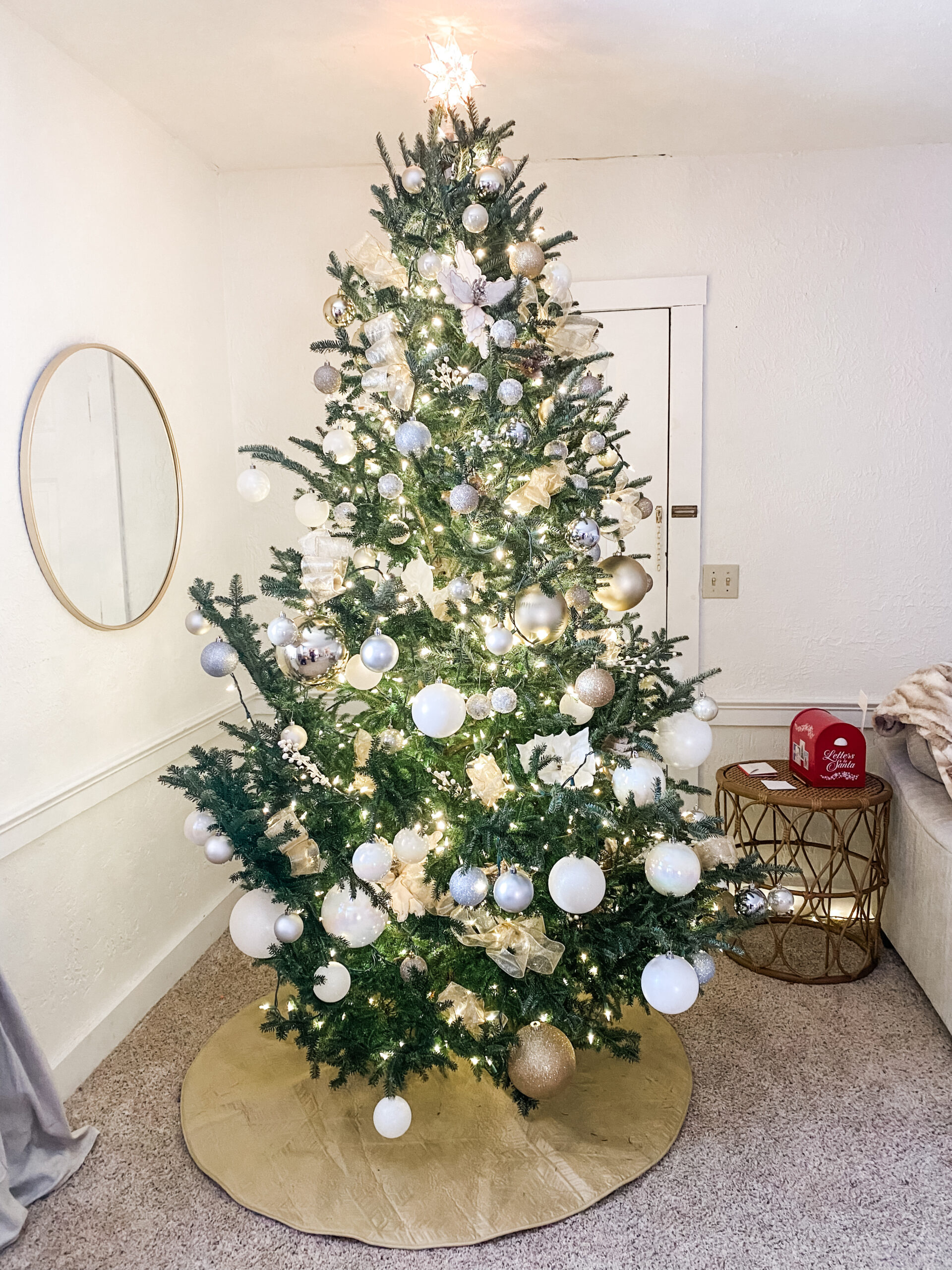 Neutral Christmas tree decorated with soft gold, white, and champagne ornaments with warm white lights and a gold tree skirt.