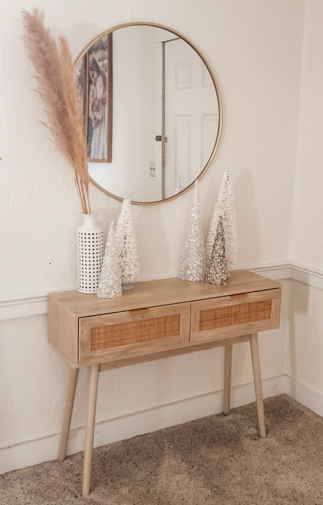 Neutral Christmas entryway with a wood console table, round mirror, pampas grass, and mini Christmas trees.
