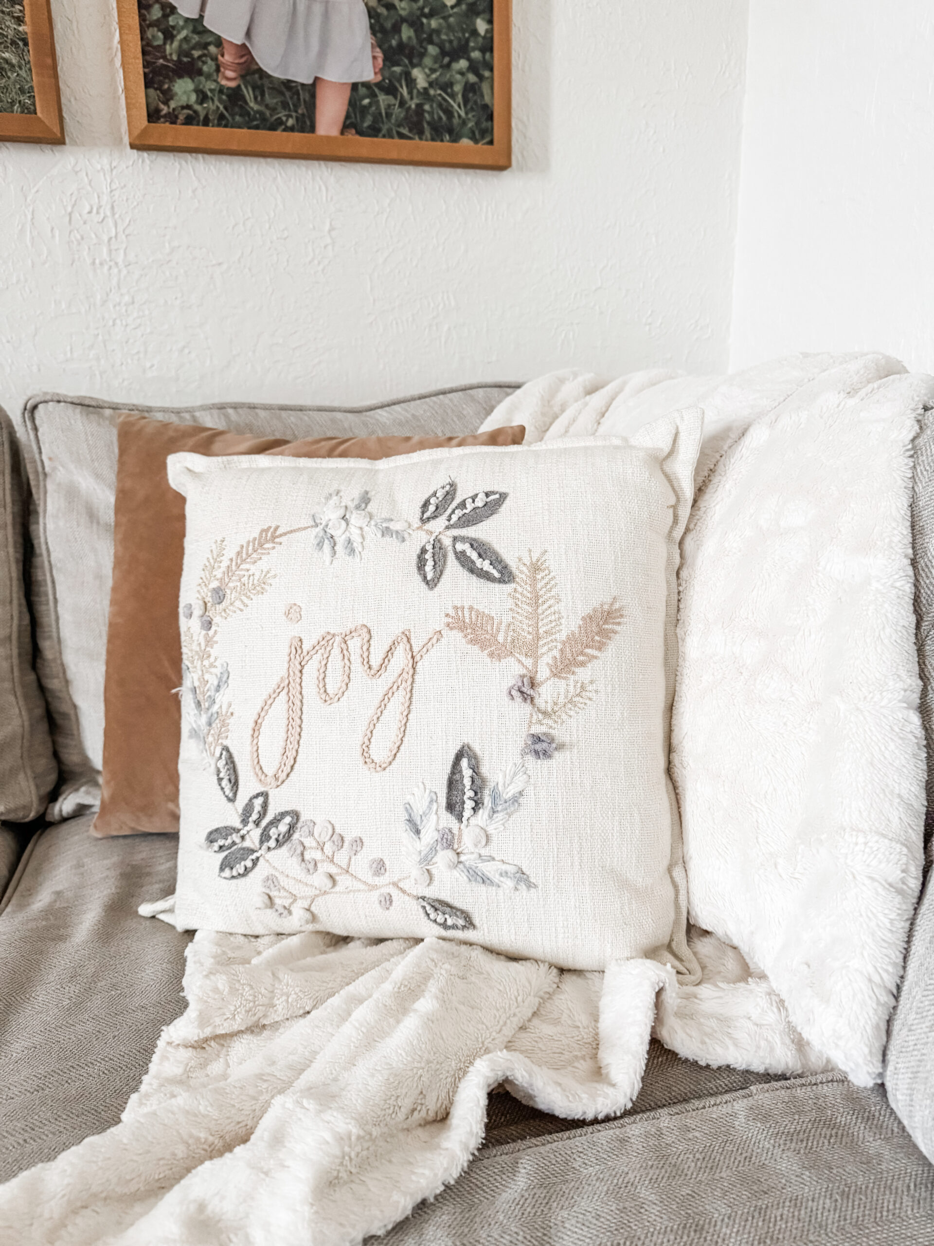 Neutral Christmas living room couch styled with a cozy throw blanket and embroidered “Joy” pillow.