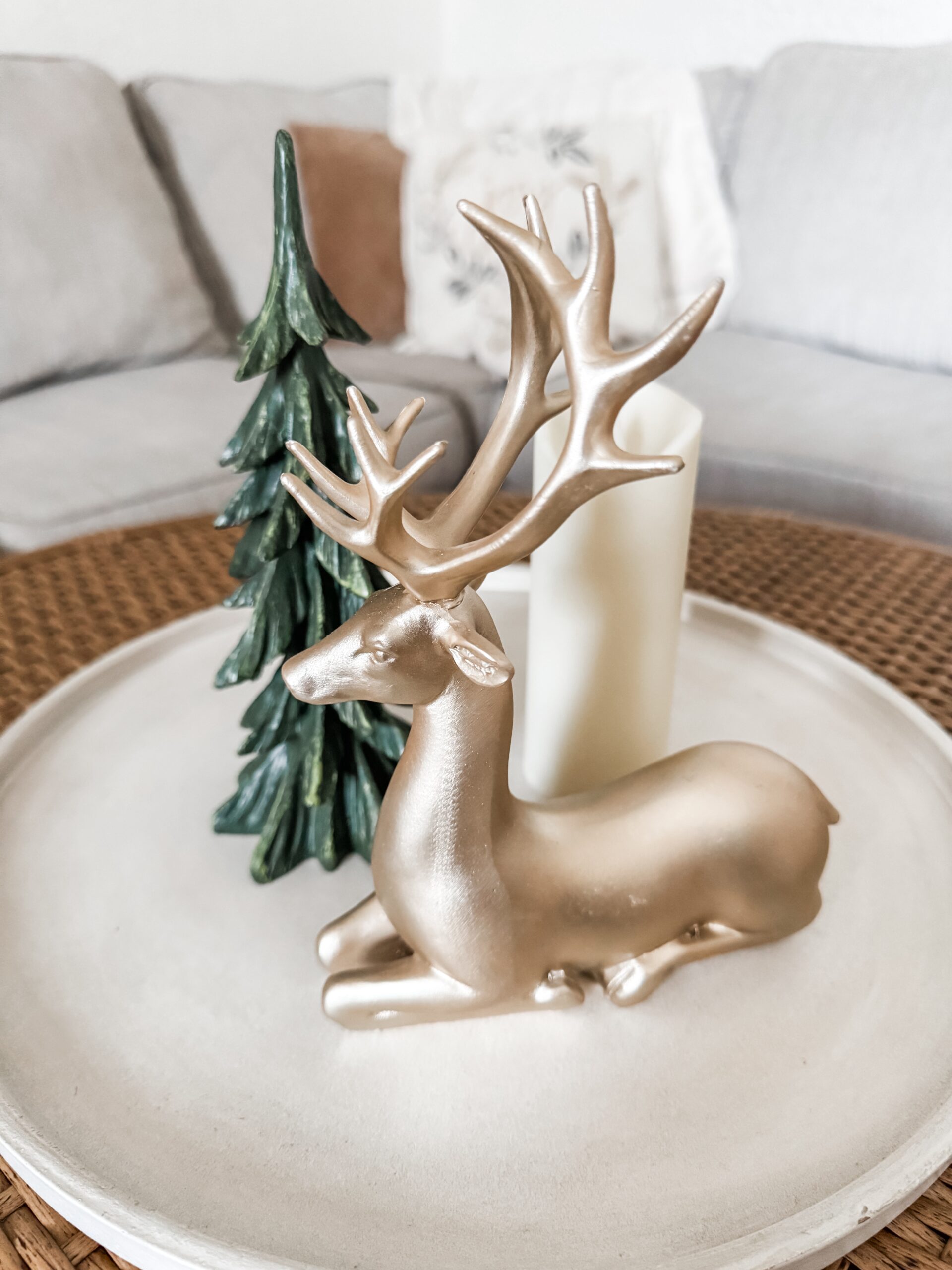 Minimal Christmas coffee table decor with a gold deer, small tree, and candle on a round tray.