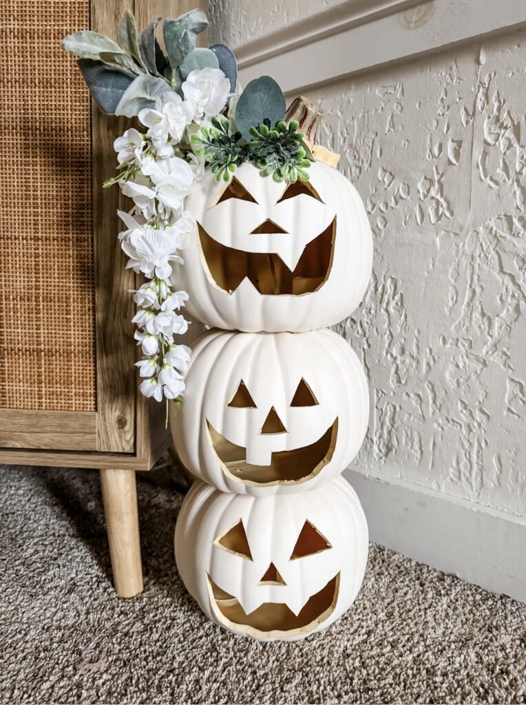 DIY Halloween decor white stacked pumpkin topiary with jack-o-lantern faces topped with faux flowers.
