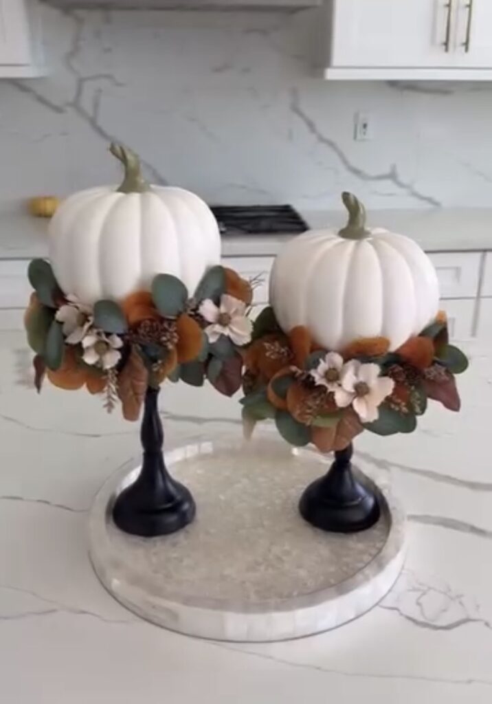White faux pumpkins elevated on black candlesticks and decorated with a wreath of autumn leaves, eucalyptus, and flowers for an easy DIY fall decor centerpiece.