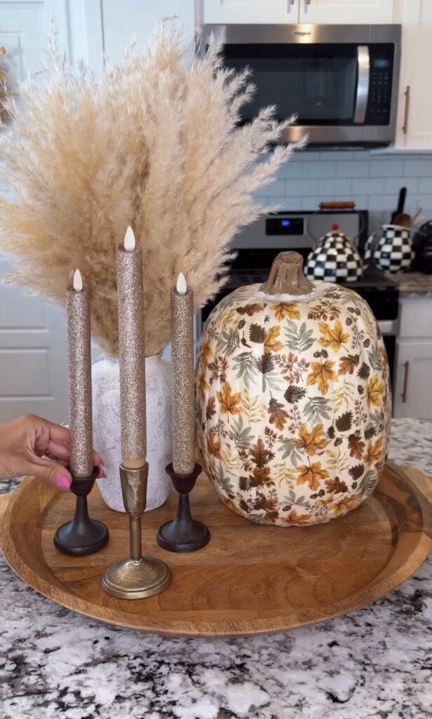 Wooden tray styled with a decoupage fall leaf pumpkin, pampas grass in a textured vase, and glitter taper candles for a cozy easy DIY fall decor display.