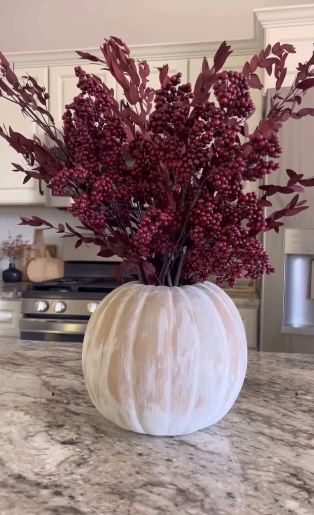 Whitewashed pumpkin vase filled with deep burgundy berry stems on a kitchen island, offering a simple easy DIY fall decor idea for autumn decorating.