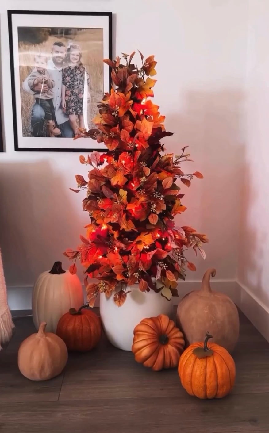 DIY fall tree decorated with orange autumn leaves and warm string lights, surrounded by assorted pumpkins for a cozy seasonal entryway display and easy DIY fall decor inspiration.