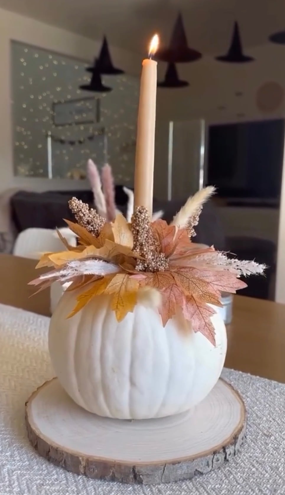 White pumpkin candle holder decorated with faux maple leaves, dried florals, and pampas grass, topped with a taper candle for an elegant easy DIY fall decor centerpiece.