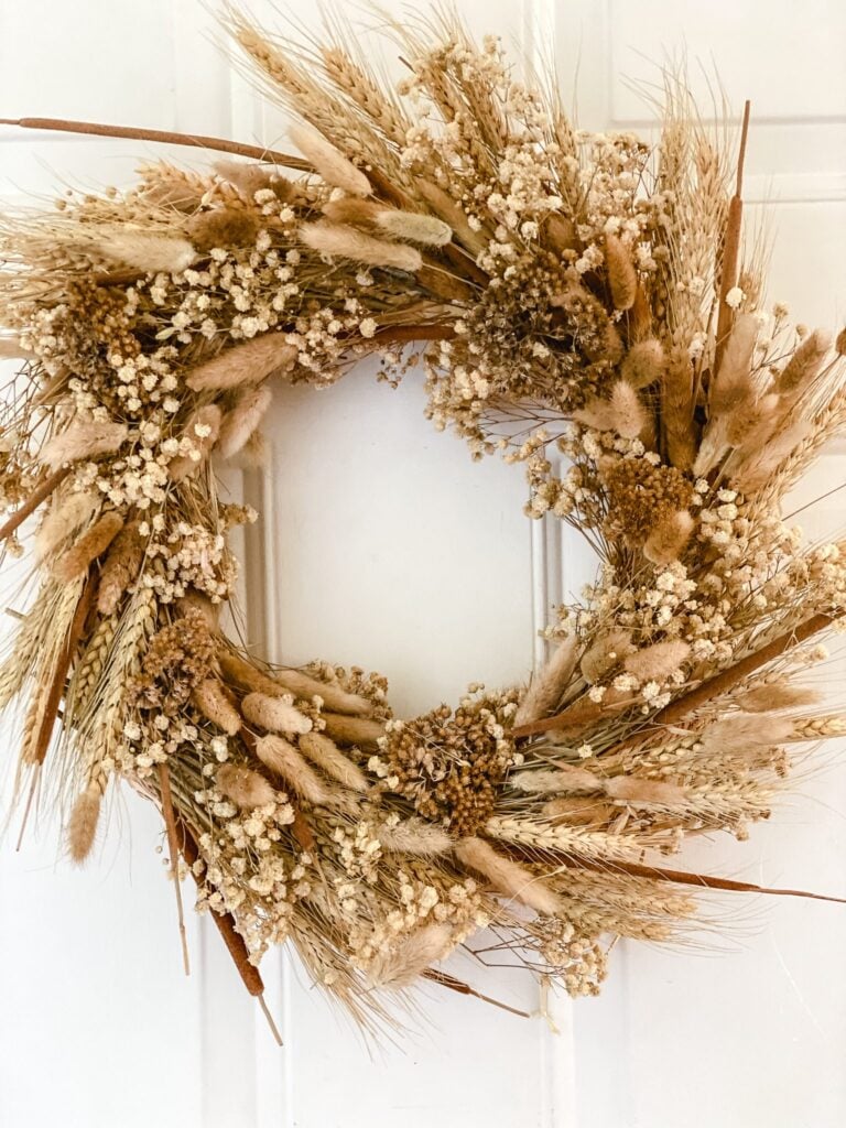 Handmade dried wheat wreath featuring bunny tails, baby’s breath, cattails, and natural grasses displayed on a white front door as easy DIY fall decor.