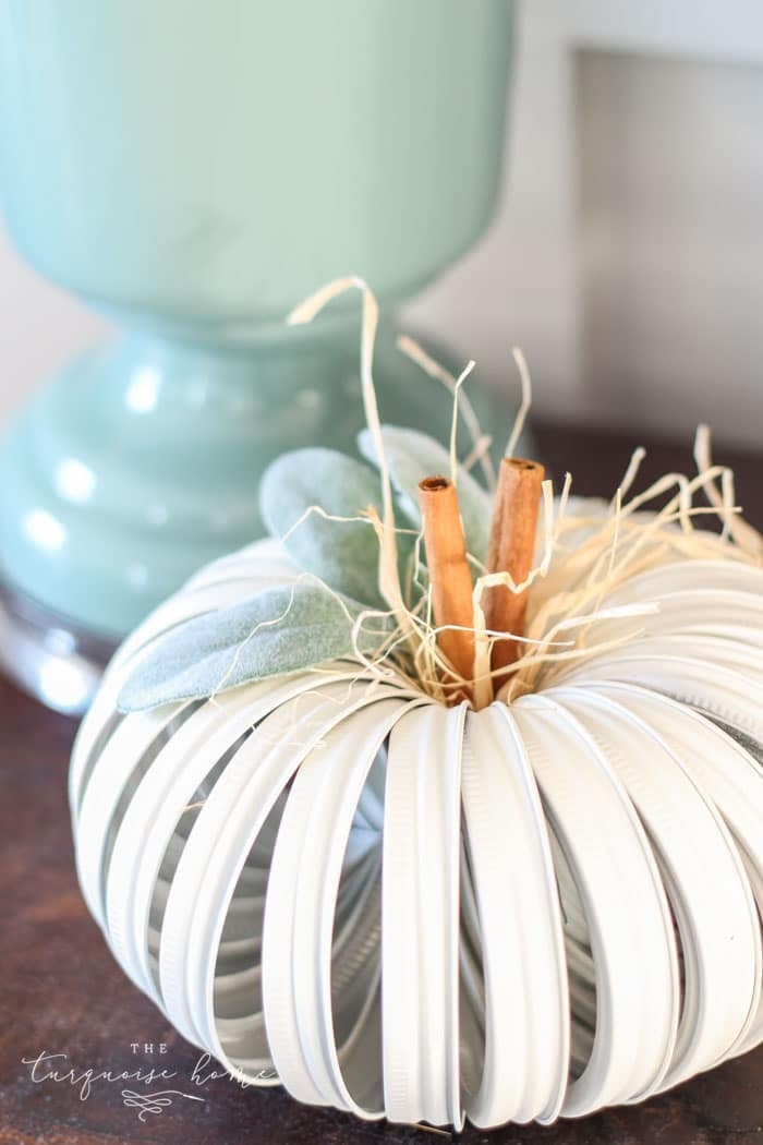 White pumpkin made from mason jar lids with cinnamon stick stems and eucalyptus leaves, creating a unique easy DIY fall decor accent.
