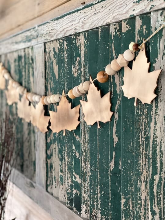 Wooden bead garland with maple leaf cutouts draped across a distressed mantel, creating simple farmhouse easy DIY fall decor.