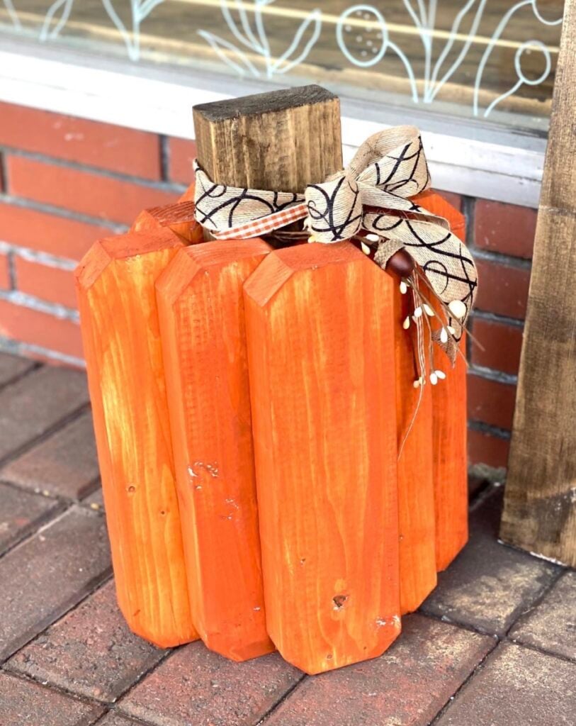 Handcrafted wooden pumpkin made from painted wood boards and finished with a decorative ribbon bow for rustic porch easy DIY fall decor.