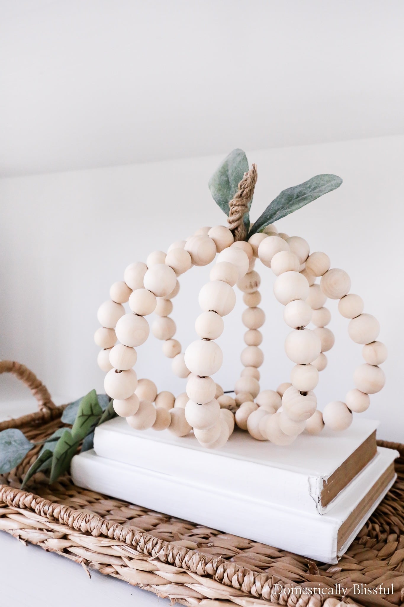 Decorative pumpkin made from unfinished wooden beads with a twine stem and eucalyptus leaves displayed on stacked books for modern easy DIY fall decor.