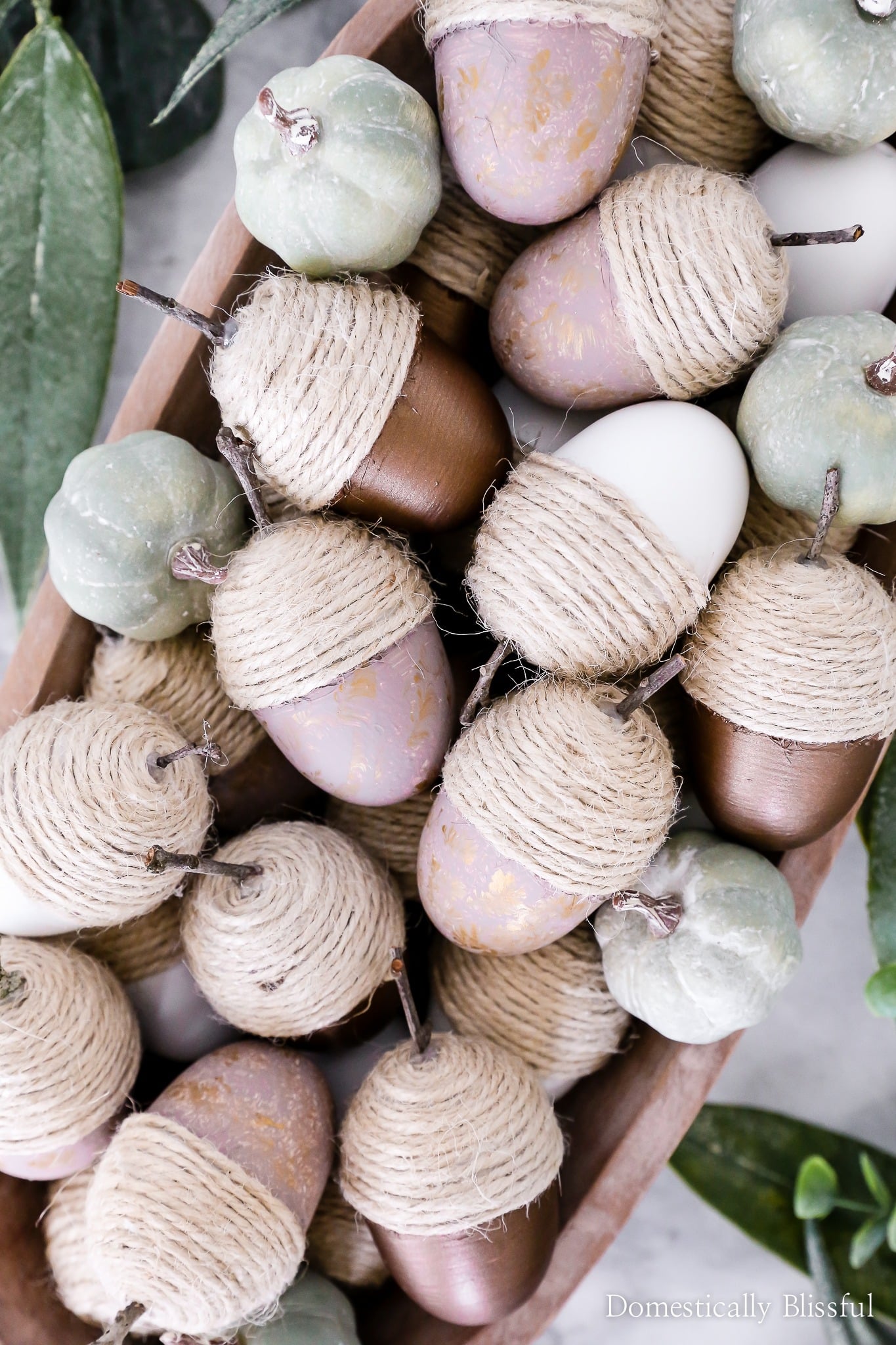 Decorative acorns wrapped with natural jute twine and painted in soft neutral colors arranged in a wooden bowl for charming easy DIY fall decor.
