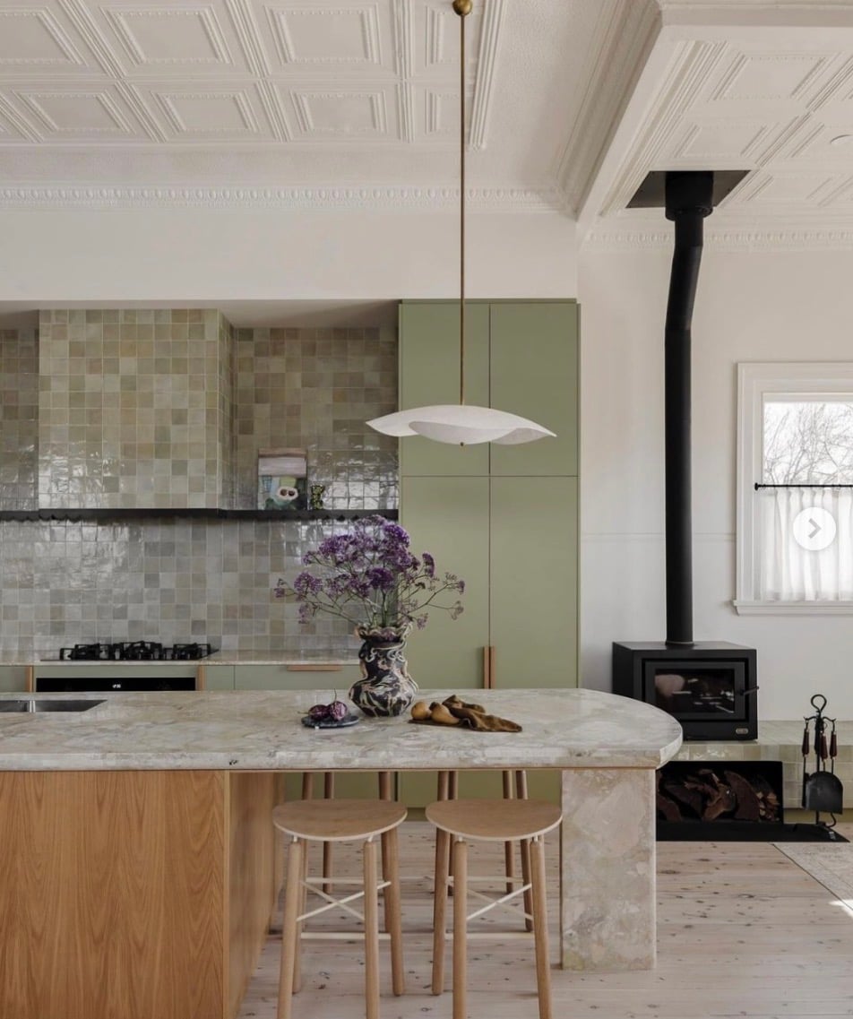 Popular kitchen backsplash idea featuring a soft green zellige tile backsplash with natural color variation, sage green cabinets, light wood accents, and a stone kitchen island.