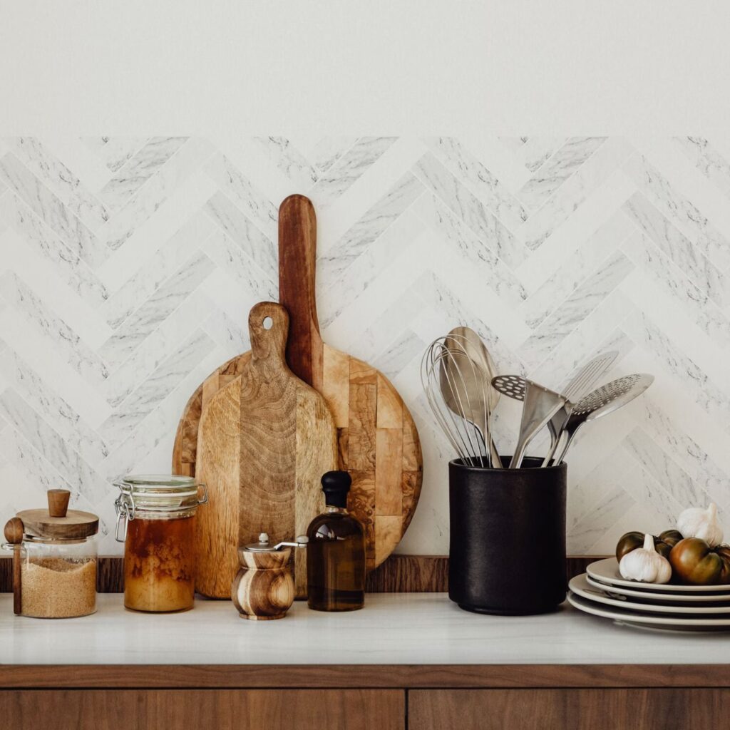 Popular kitchen backsplash idea featuring white and gray marble tile arranged in a herringbone pattern, paired with warm wood accents and a white countertop.