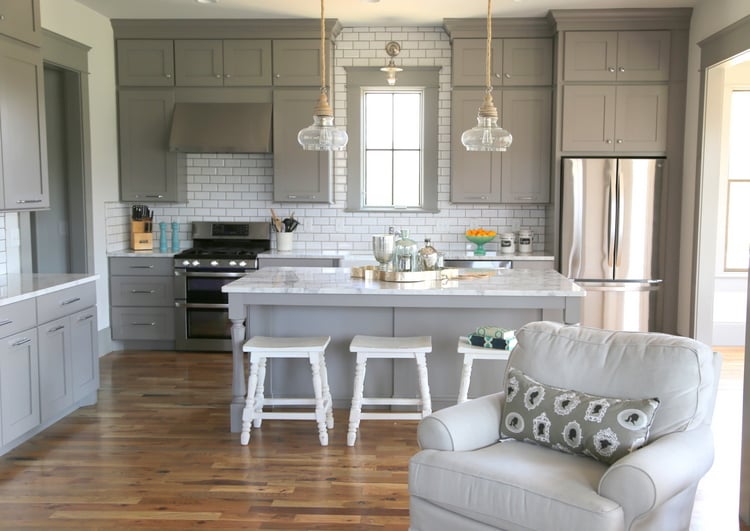 Popular kitchen backsplash idea featuring white subway tile extending to the ceiling, paired with warm gray cabinets, white countertops, and a large kitchen island.