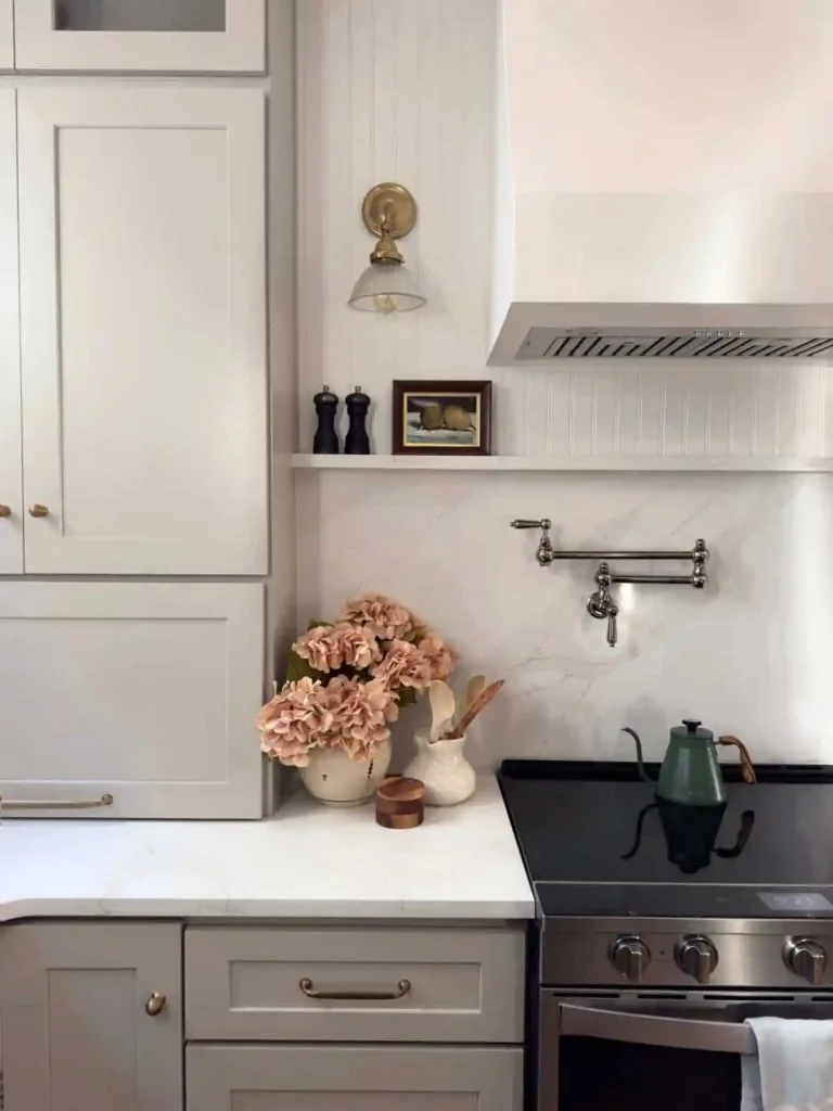Popular kitchen backsplash idea featuring a seamless white marble backsplash with subtle gray veining, paired with warm white cabinets, brass accents, and a stainless steel range.