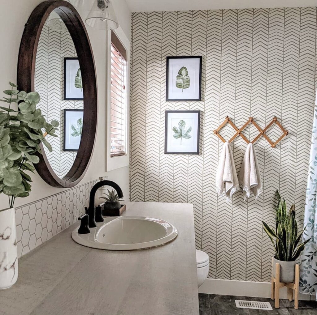 Hand-stamped herringbone accent wall in a bright bathroom with botanical artwork, wood accents, greenery and neutral decor.