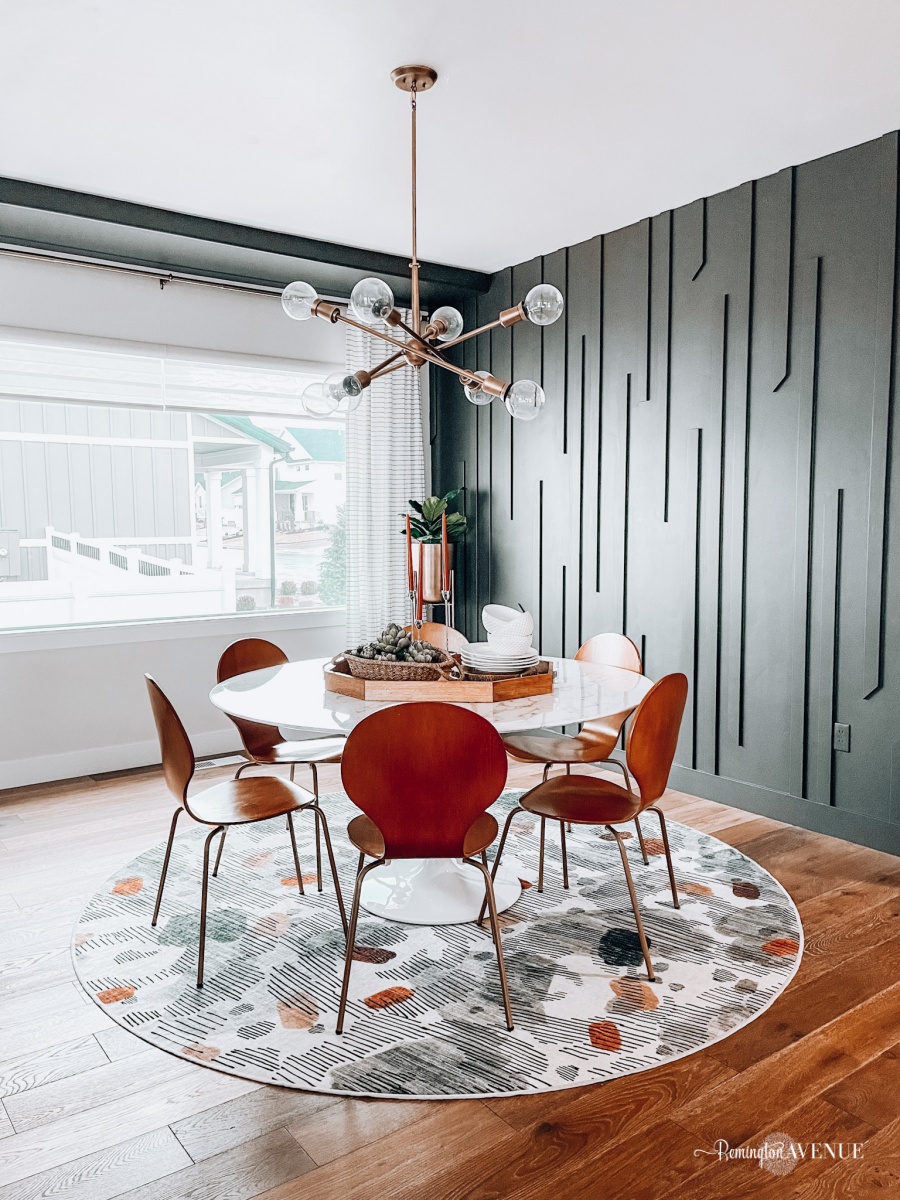 Dark green midcentury modern accent wall with geometric vertical wood trim in a dining room with a round table and wood chairs.