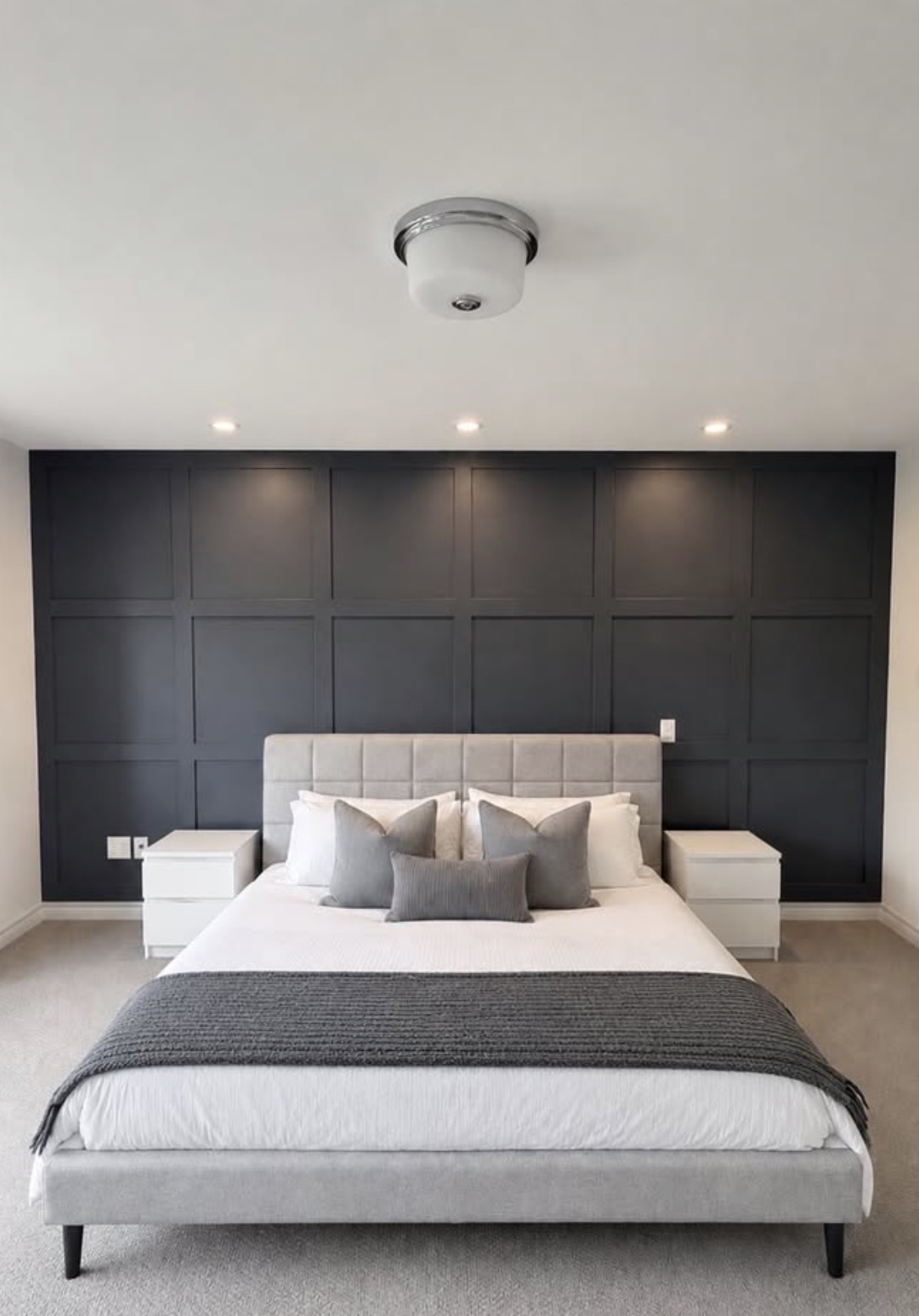 Moody dark navy board and batten accent wall behind a bed in a modern bedroom with white and gray neutral decor.