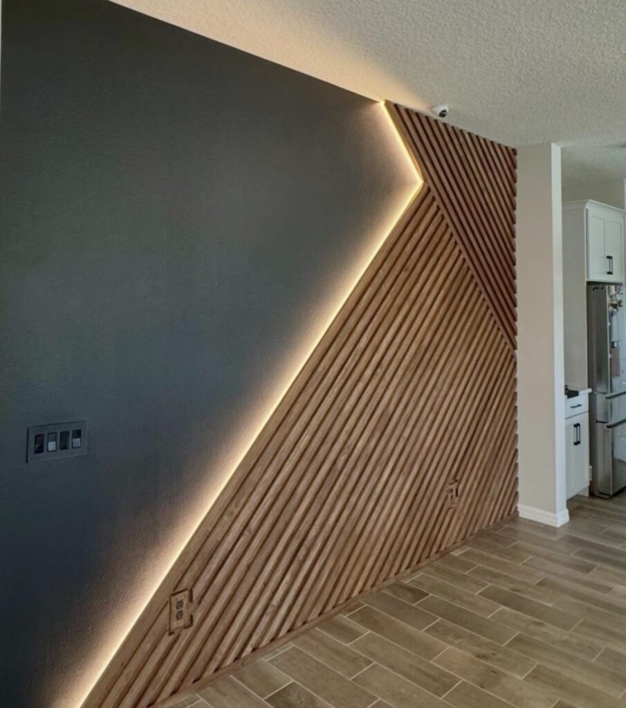 Modern diagonal wood slat accent wall with warm LED backlighting against a dark gray wall for a sleek, contemporary look.