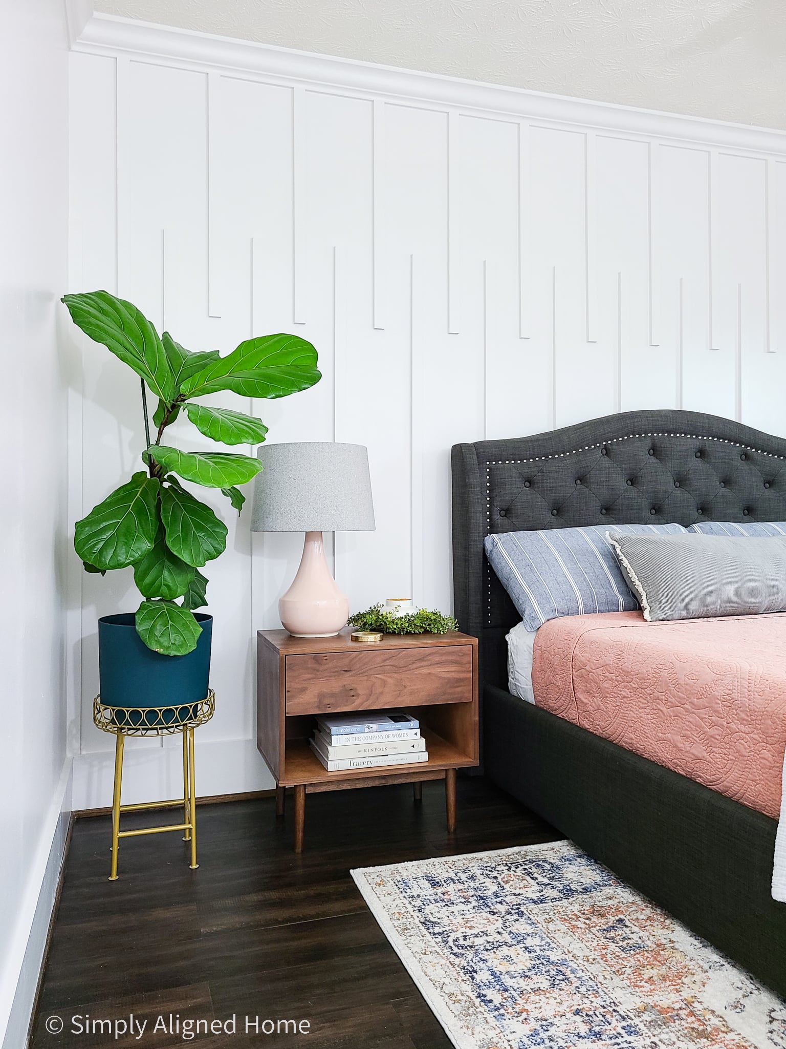 White modern linear molding accent wall in a bedroom with a dark tufted bed, midcentury wood nightstand and colorful decor.