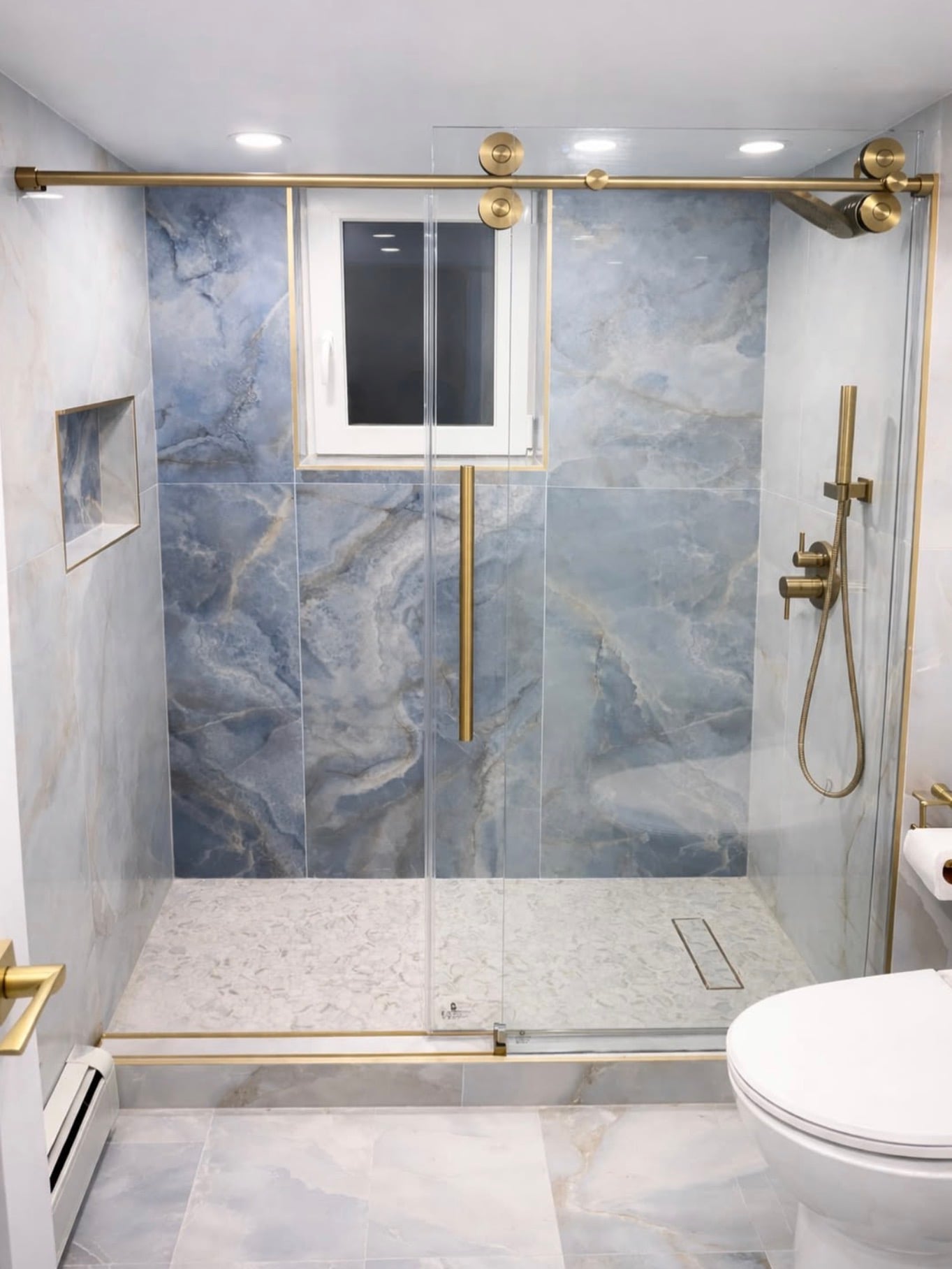 Luxury walk-in shower with large-format blue marble-look accent wall tiles, white marble-look side walls, brushed gold shower fixtures, gold-framed sliding glass doors, and white mosaic tile flooring.